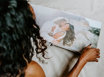 Woman flipping through Signature Layflat Wedding Album opened to two page panoramic image of bride and groom