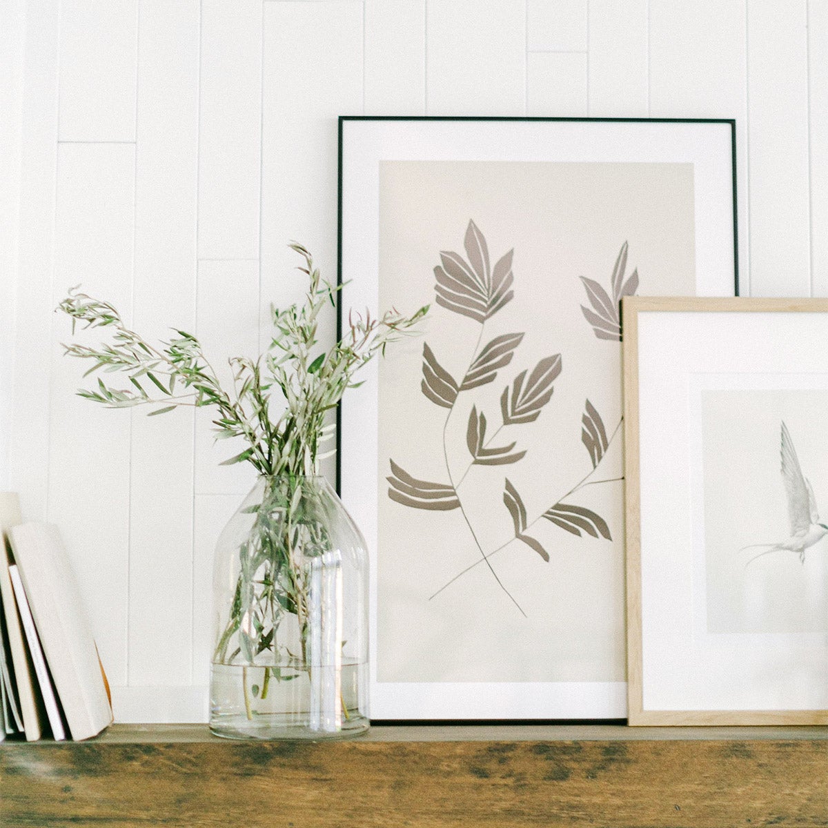 Two frames layered on mantle next to vase of foliage
