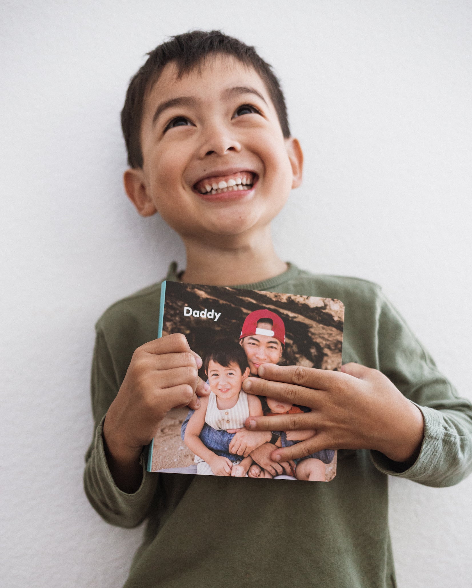 Little boy holding up Artifact Uprising Board Book titled Daddy