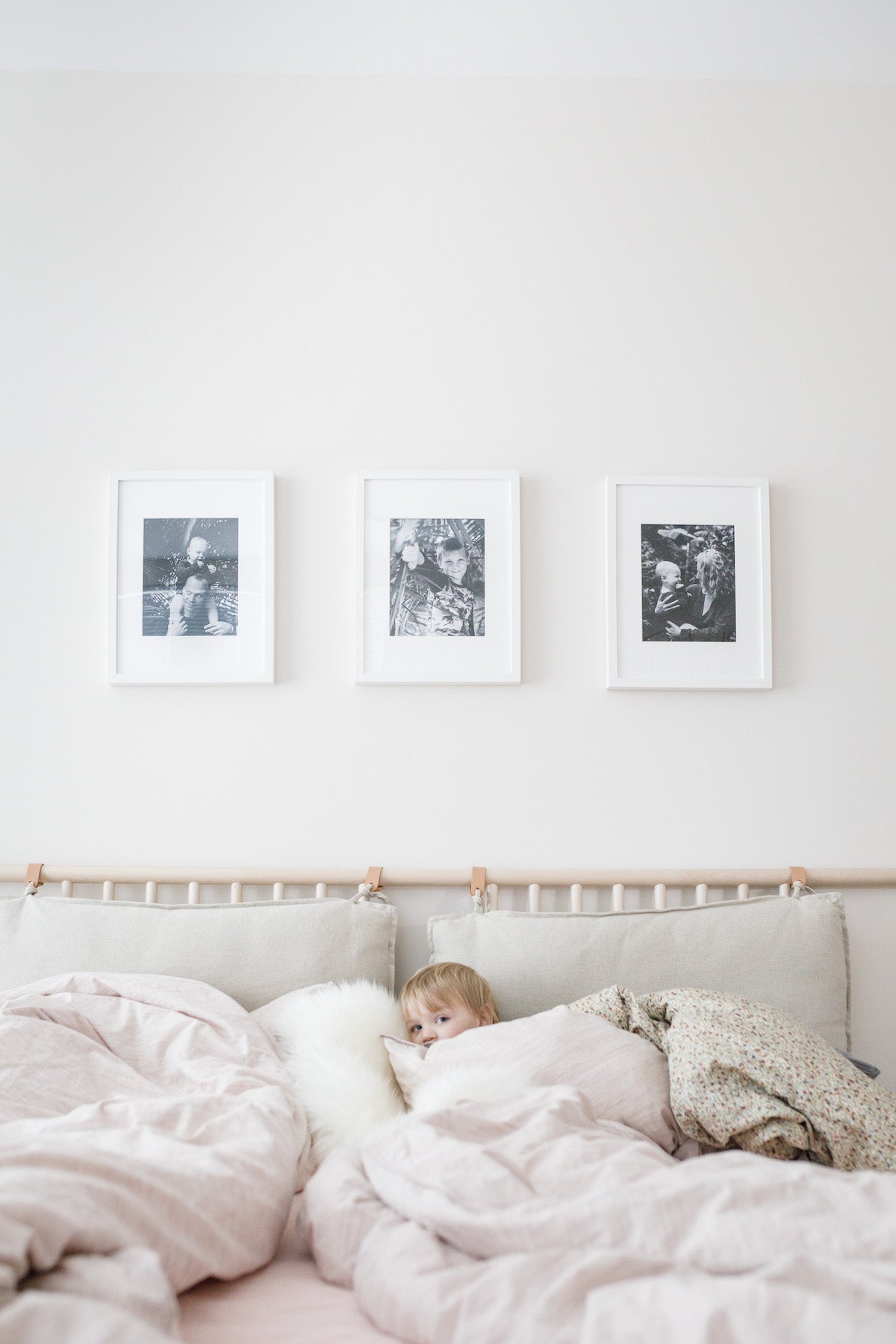 Child curled up under blankets with three Artifact Uprising Gallery Frames filled with family photos overhead.