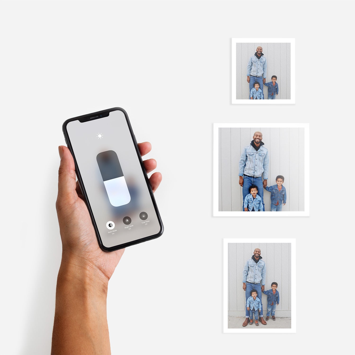 Hand adjusting screen brightness on an iphone next to three Artifact Uprising photo prints featuring family photos of a father and their children