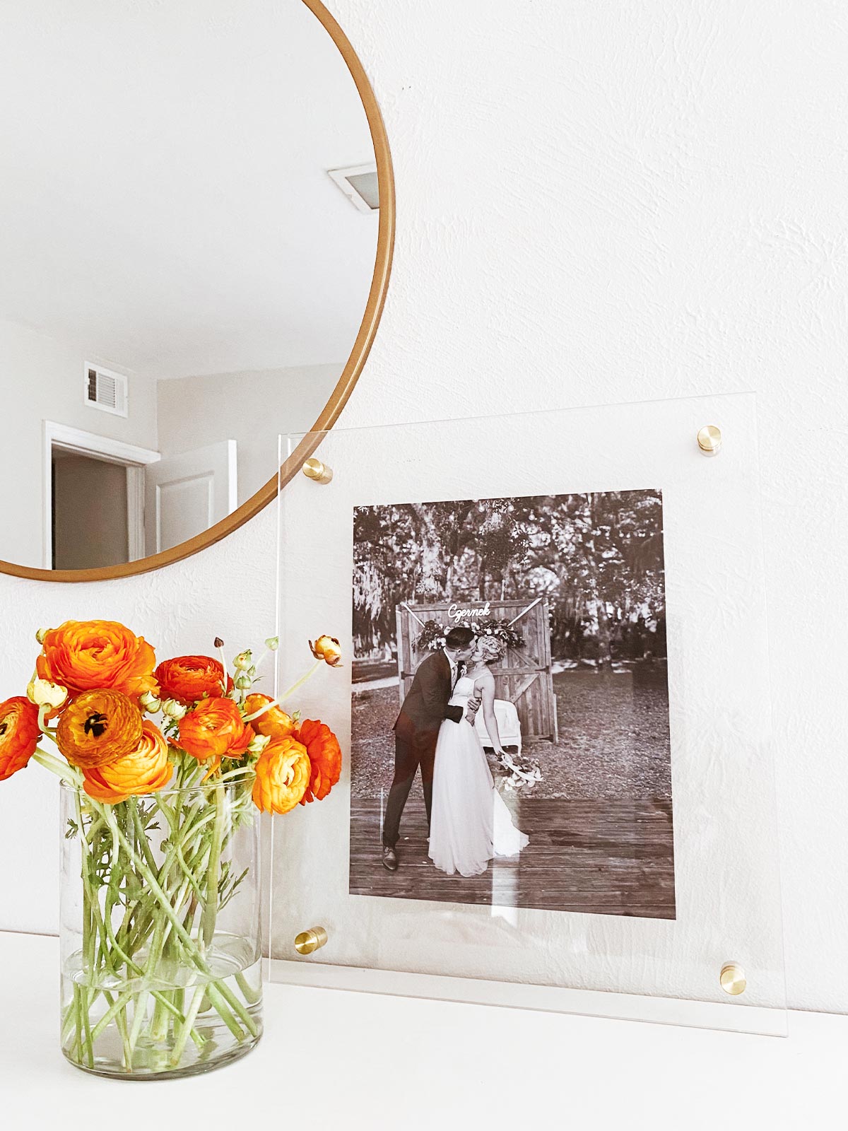 An Artifact Uprising Floating Frame featuring a wedding photo leaning against the wall on a dresser next to a brass mirror and summery bouquet