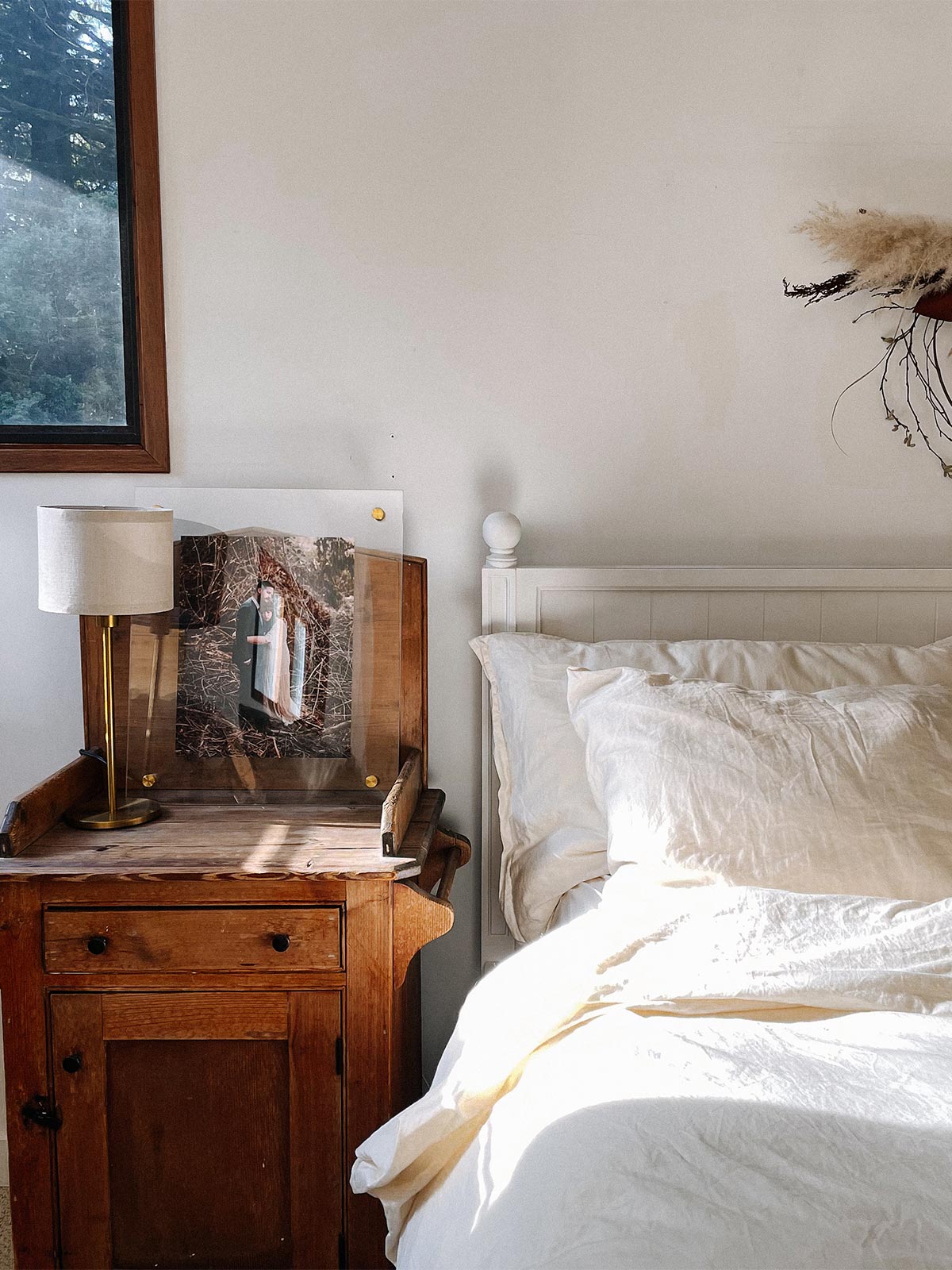 An Artifact Uprising Floating Frame resting against the wall on the nightstand next to a bed with white linens