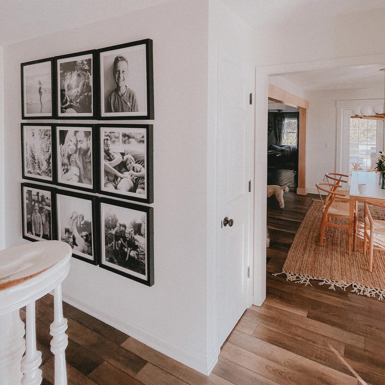 A clean, light-filled hallway with a gallery wall grid of black Artifact Uprising Gallery Frames featuring black and white family photos
