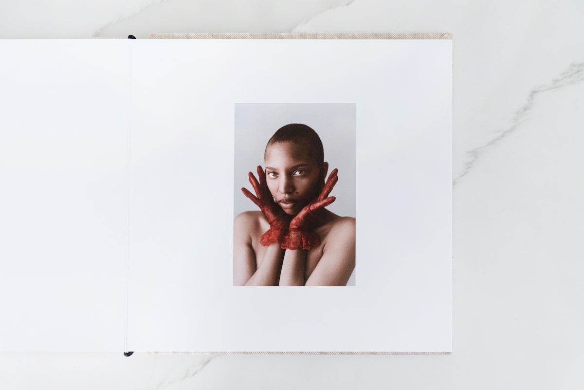 Artifact Uprising Layflat Photo Album opened to portrait of woman in red gloves on right page and blank left page