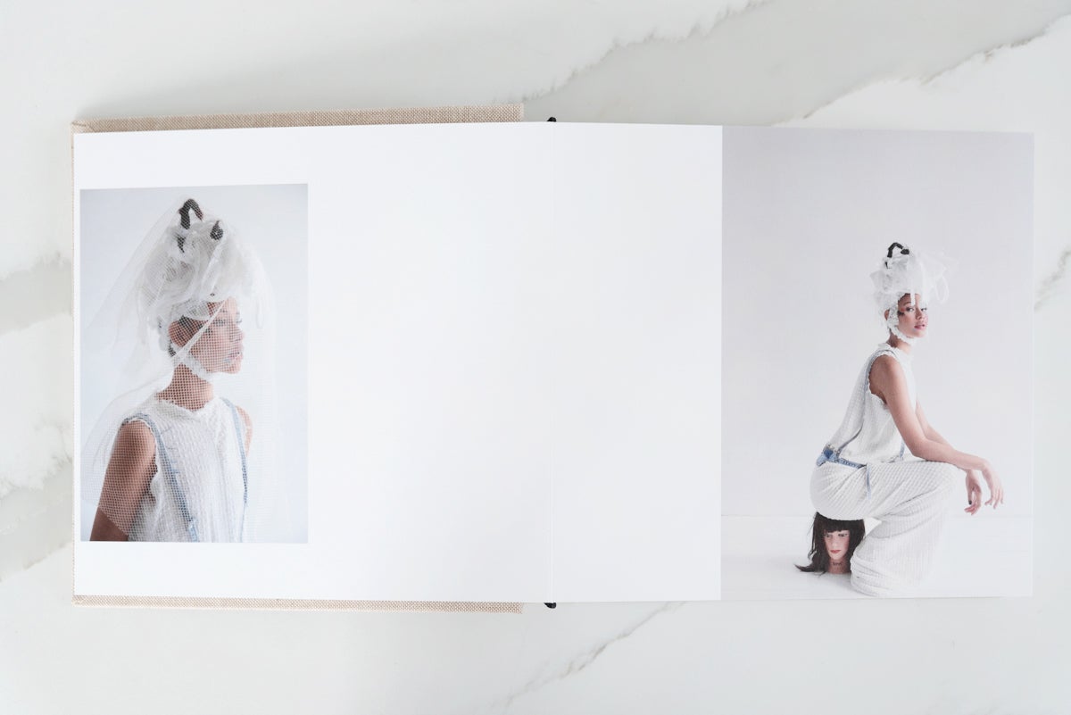 Artifact Uprising Layflat Photo Album opened to portrait of woman wearing veil on left page and same woman sitting on a manikin head on right page