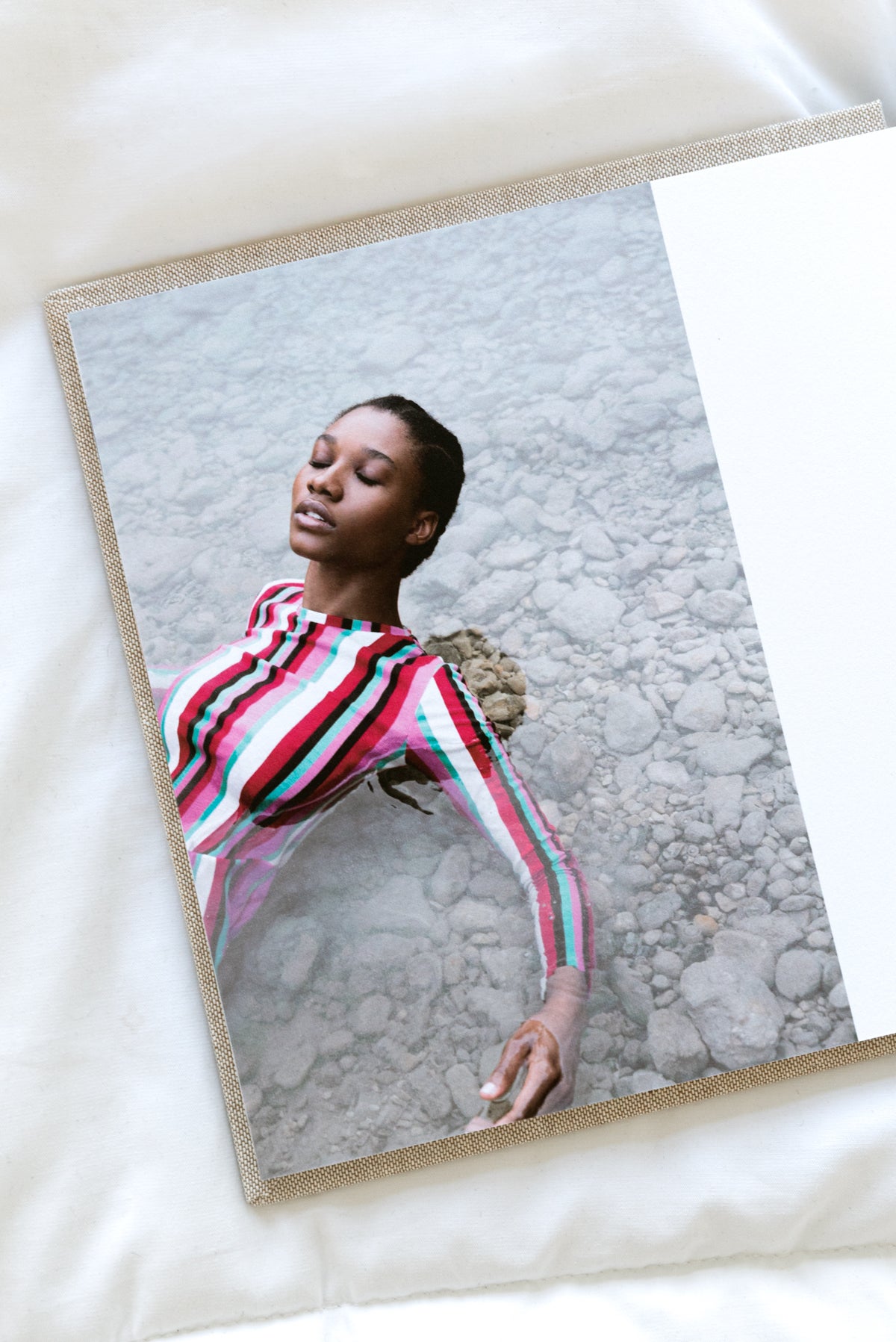 Artifact Uprising Layflat Photo Portfolio Book opened to portrait of young women in long-sleeve striped dress laying in shallow water