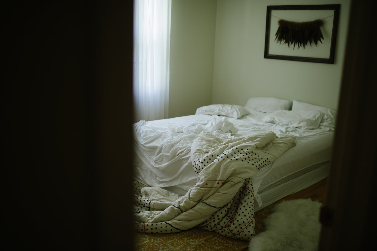 Photo by Martha Swann-Quinn of empty bed visible through crack in the door