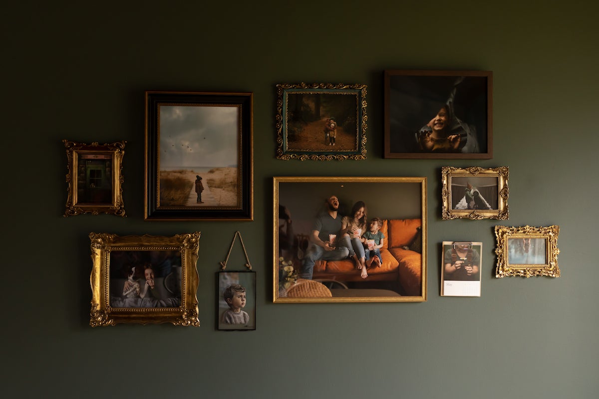 Gallery wall featuring family photos in gold and brass frames hung on dark olive green wall