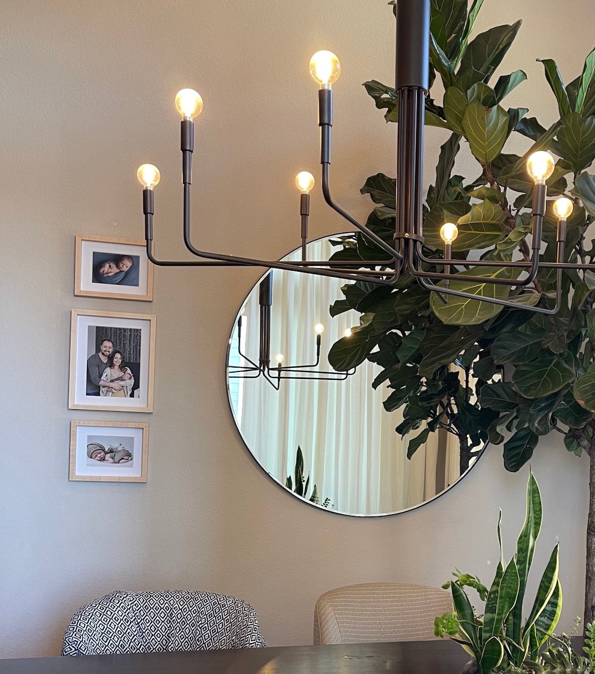 An Artifact Uprising Wooden Tabletop Frames hung in vertical trio on dining room wall next to circular mirror behind a modern chandelier