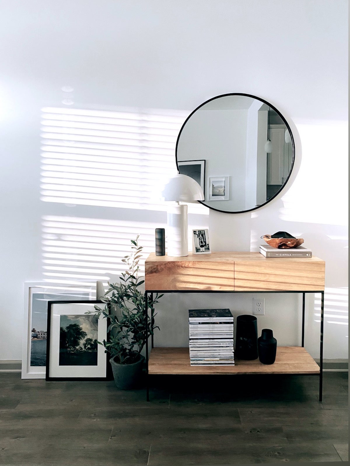 Two large Artifact Uprising Gallery Frames on the ground layered one in front of the other against the wall next to a credenza, house plant, and mirror