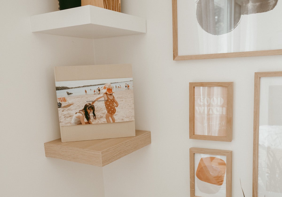 Artifact Uprising Hardcover Photo Book featuring photo of tow little girls at the beach placed on small corner wall shelf next to gallery wall of frames