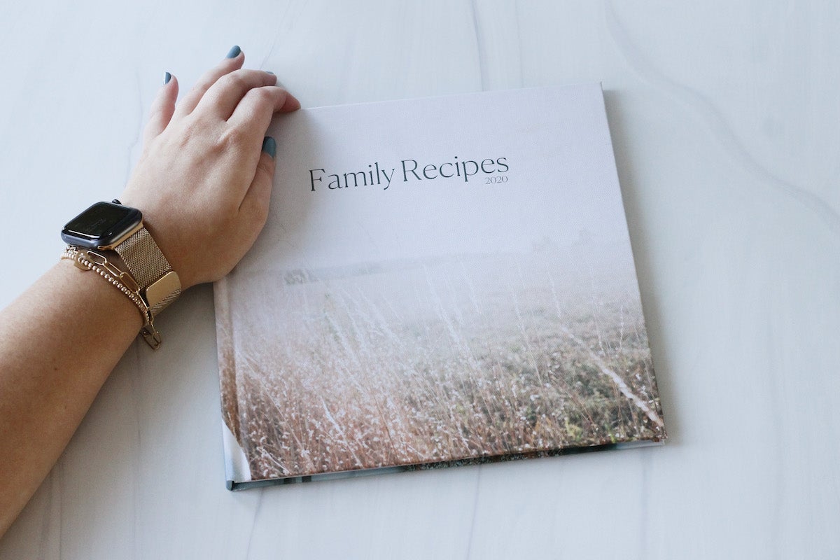 Woman's hand resting on Artifact Uprising Photo-Wrapped Hardcover book titled family recipes