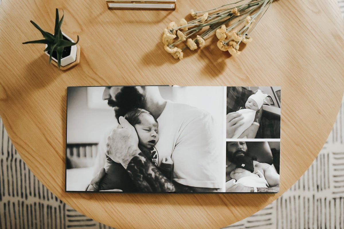 Artifact Uprising Layflat Photo Album on coffee table opened to photos of father holding newborn