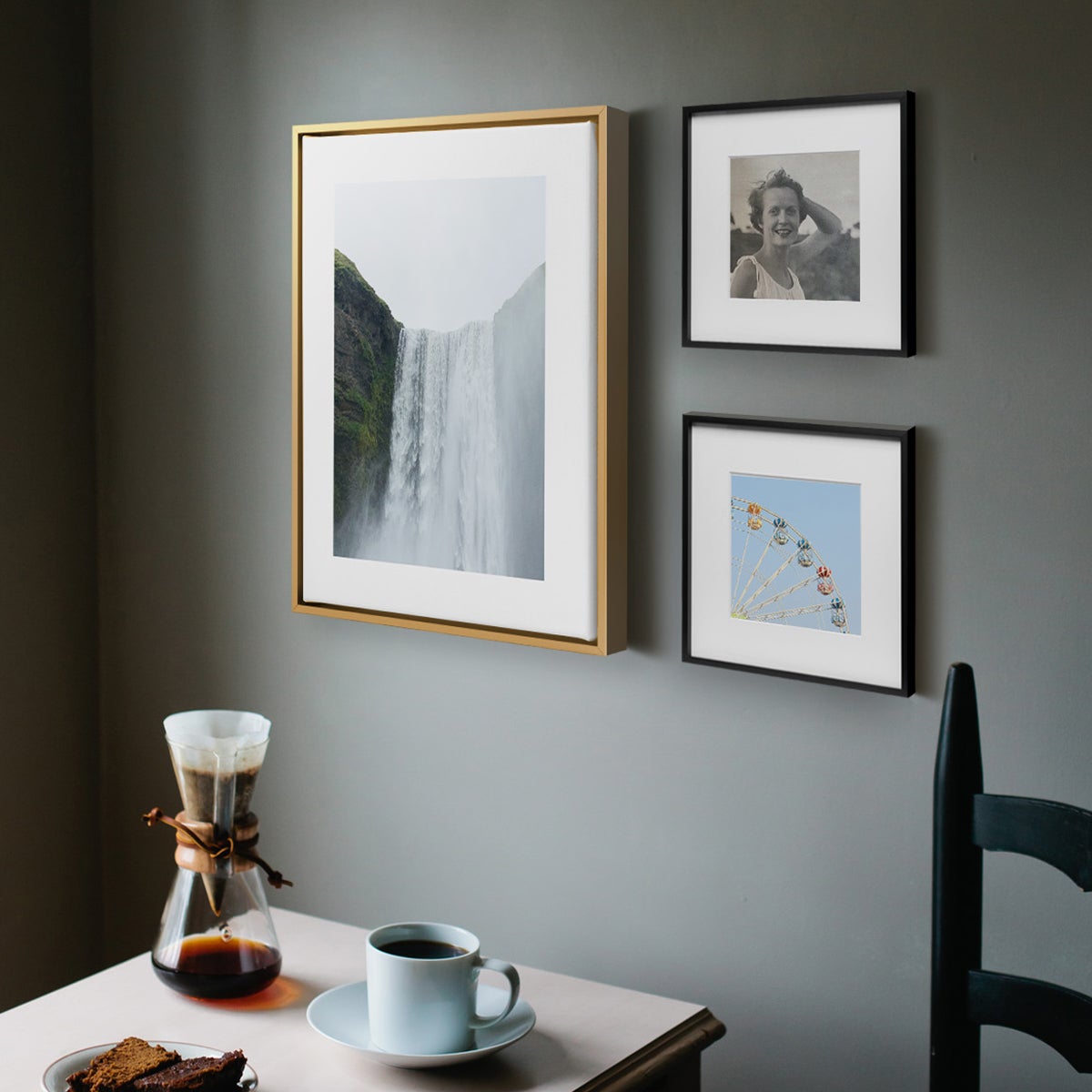 Two identical Black Artifact Uprising Modern Metal Frames hung vertically to the right of Brass Framed Canvas Print and above small nook table