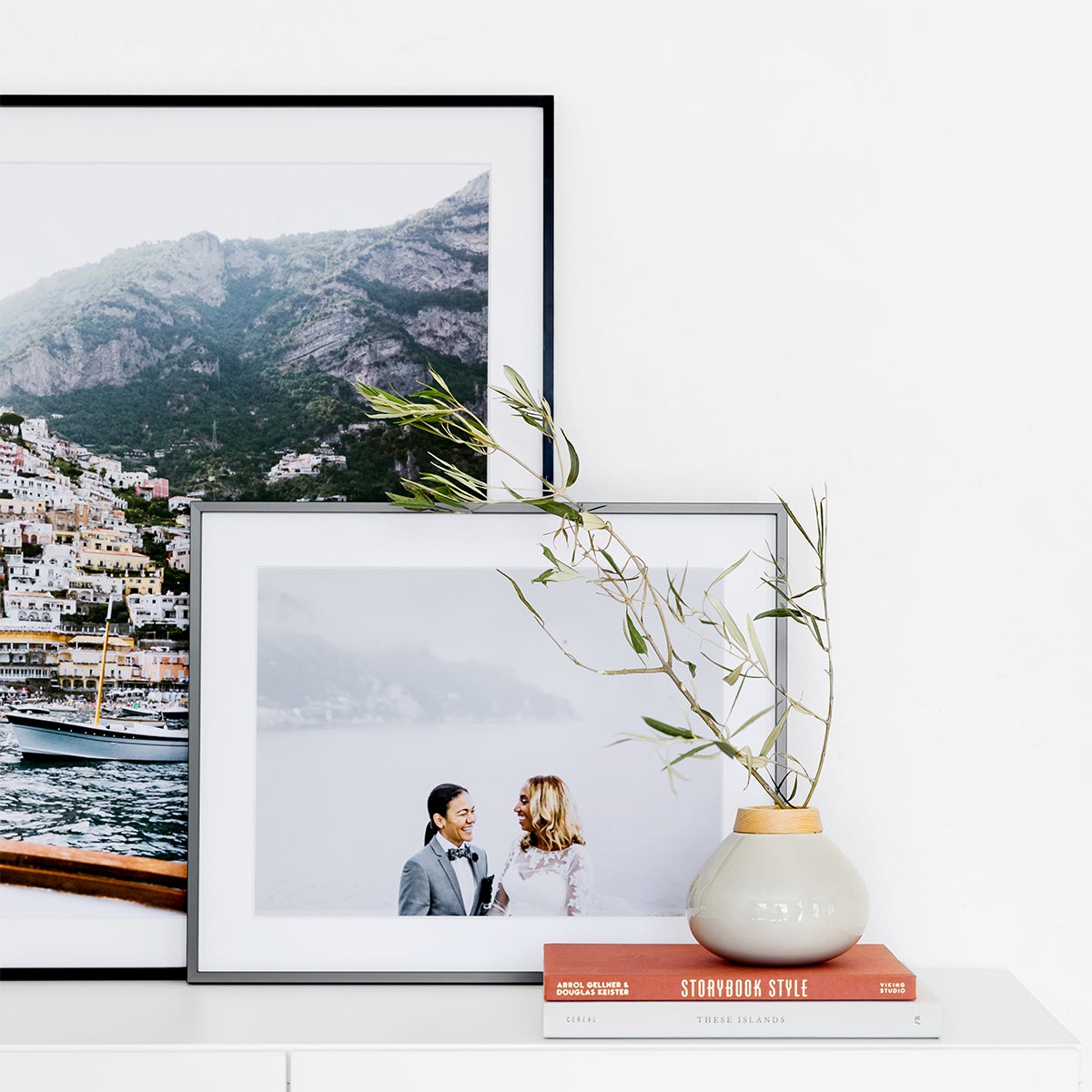 Two Artifact Uprising Modern Metal Frames in diffrent sizes and finishes layered one in front of the other on mantel next to small plant atop two small stacked books