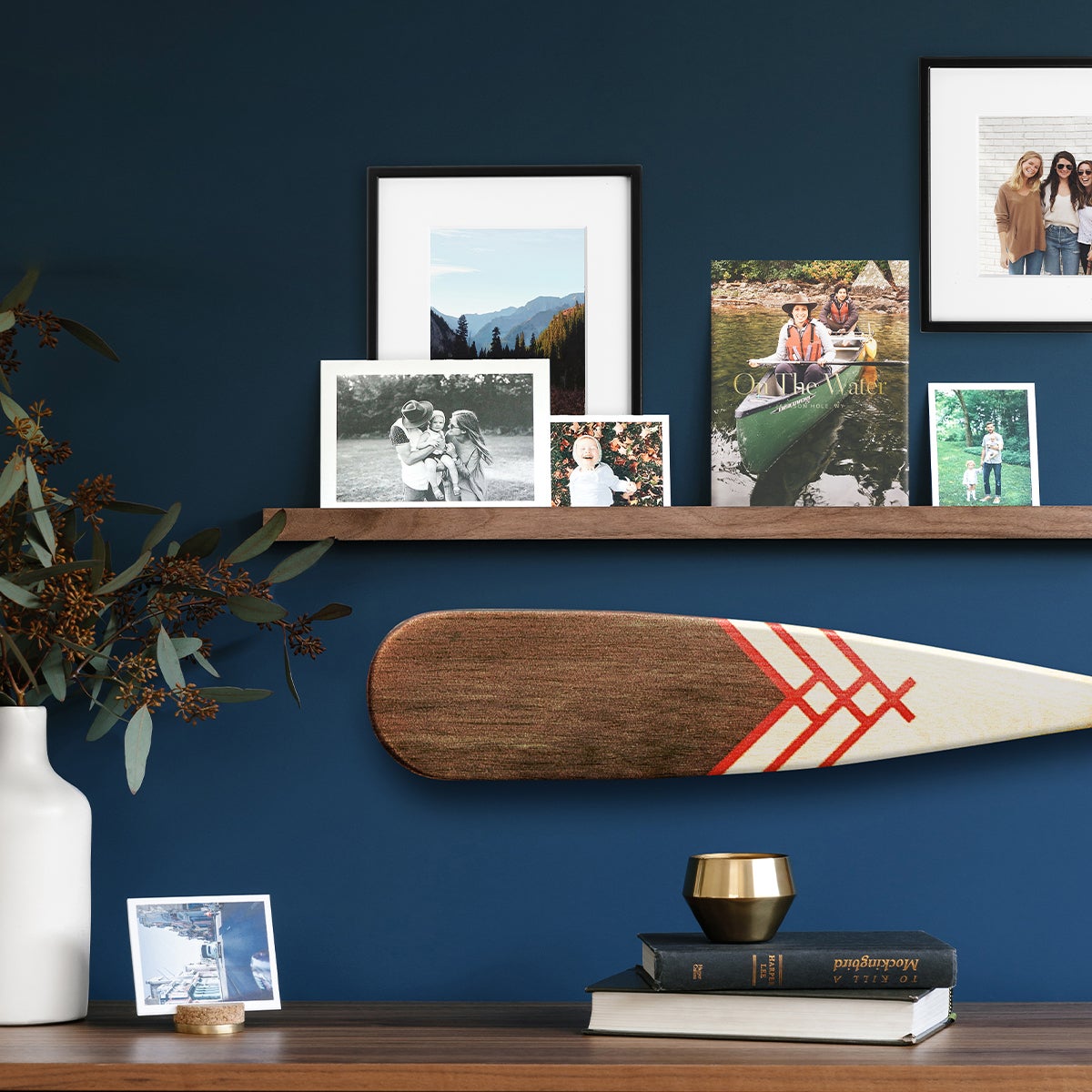 Artifact Uprising Metal Wooden Photo Ledge hung on royal blue wall and adorned with prints, frames, and photo books