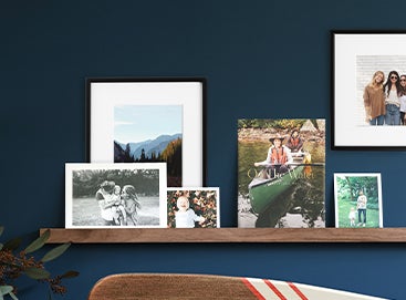 A wooden ledge styled with layers of photo prints, books, and frames.