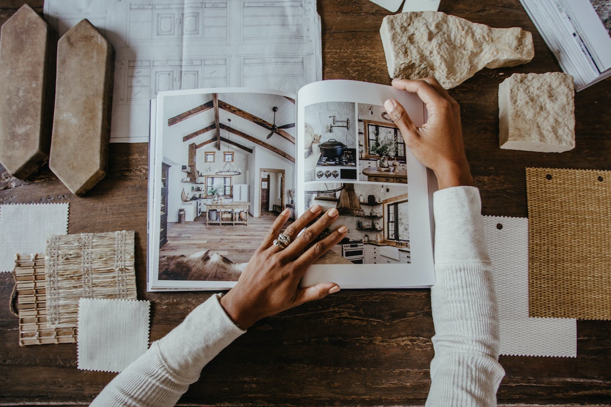 Hands flipping through photos of home renovation printed in Artifact Uprising Hardcover Photo Book on table surrounded by samples of tile and other finishings