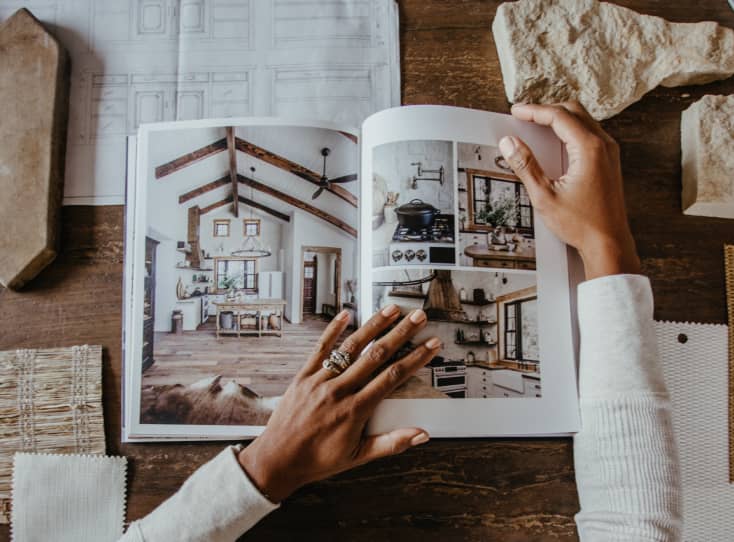 Hands flipping through photos of home renovation printed in Artifact Uprising Hardcover Photo Book on table surrounded by samples of tile and other finishings