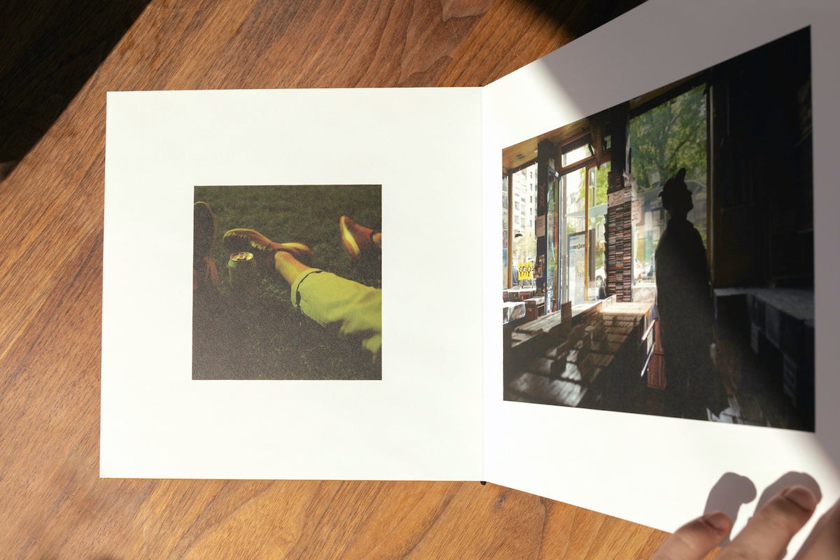 Woman's hand flipping to next page in Artifact Uprising Layflat Photo Album opened to image of man in record store