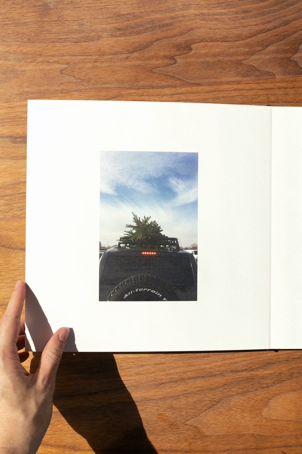 Artifact Uprising Layflat Photo Album opened to photo of pine tree strapped to the top of a Jeep