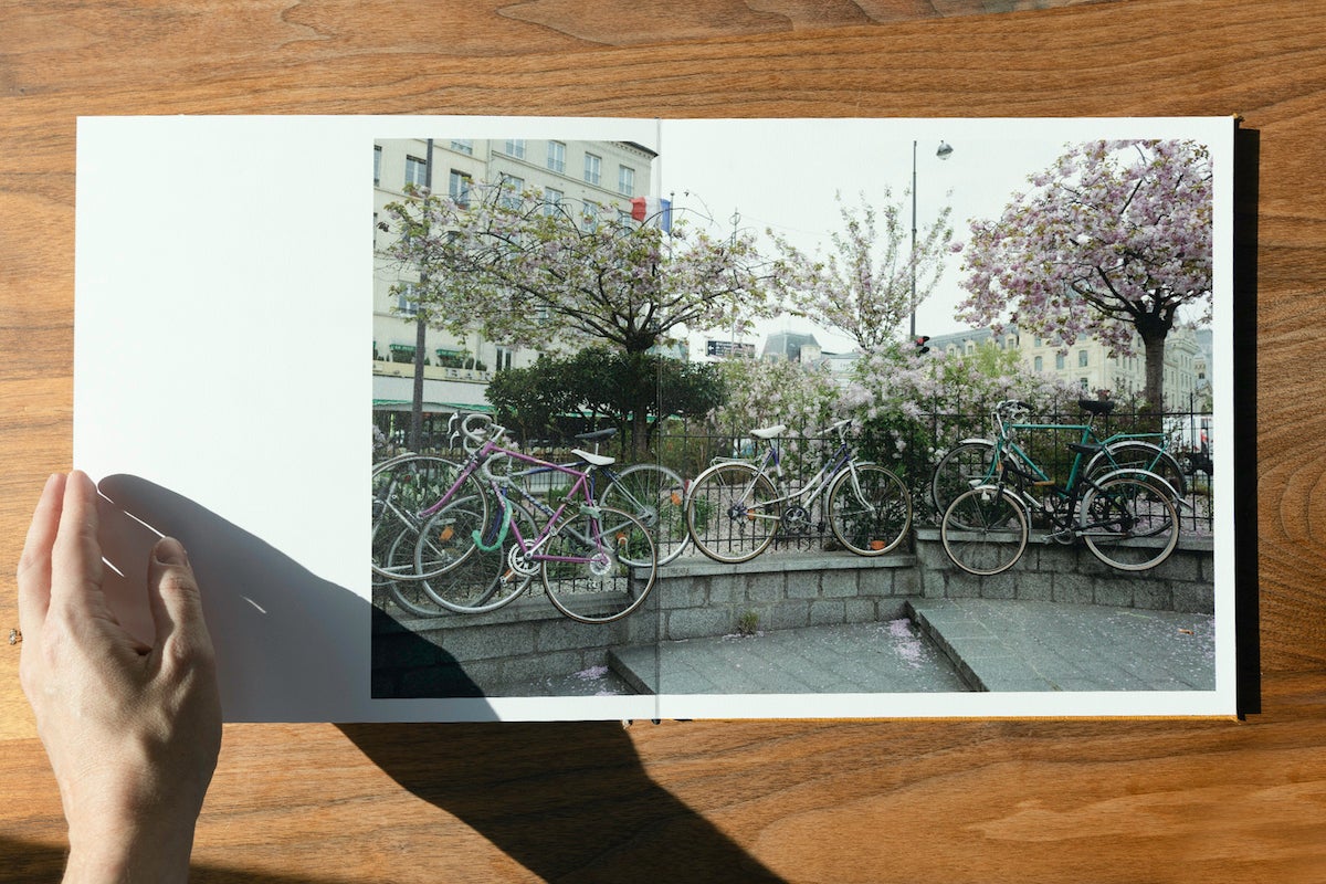 Woman's hand resting on Artifact Uprising Layflat Photo Album opened to photos of colorful bikes along railing