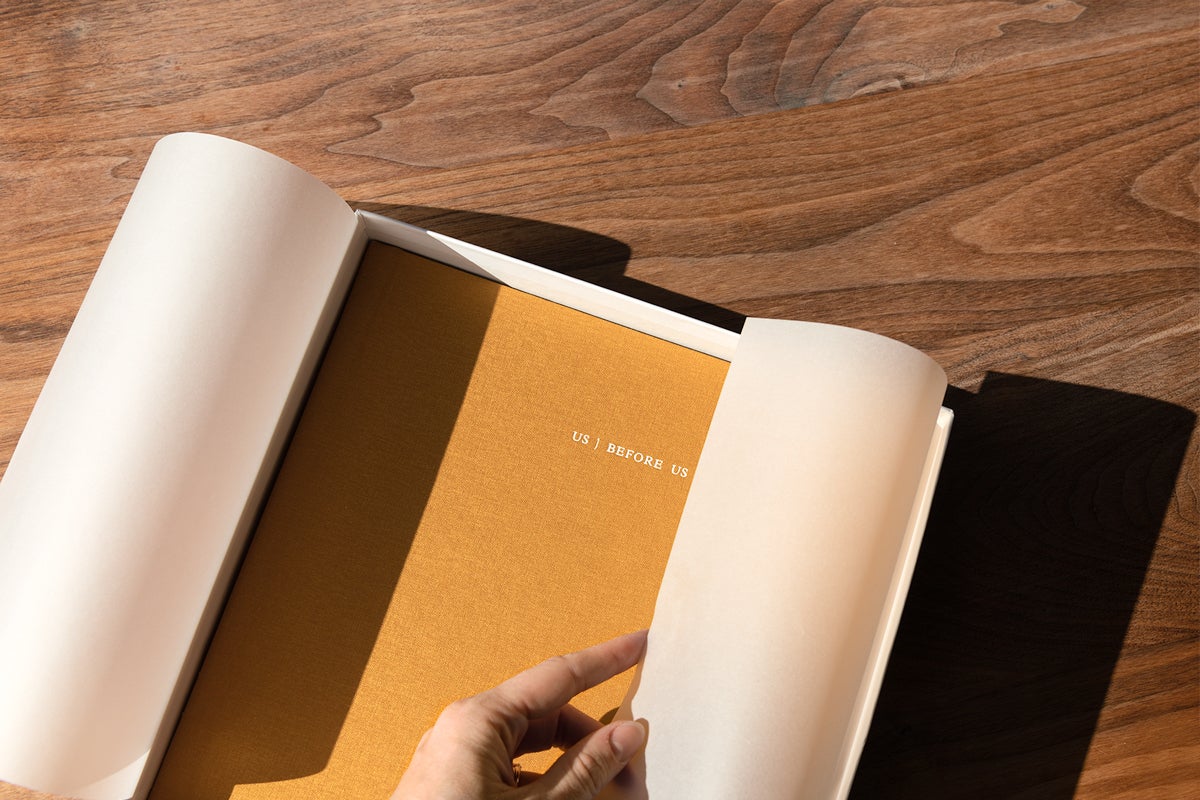 Woman's hand pulling back tissue paper to reveal cover of honeycomb Artifact Uprising Layflat Photo Album titled Us Before Us