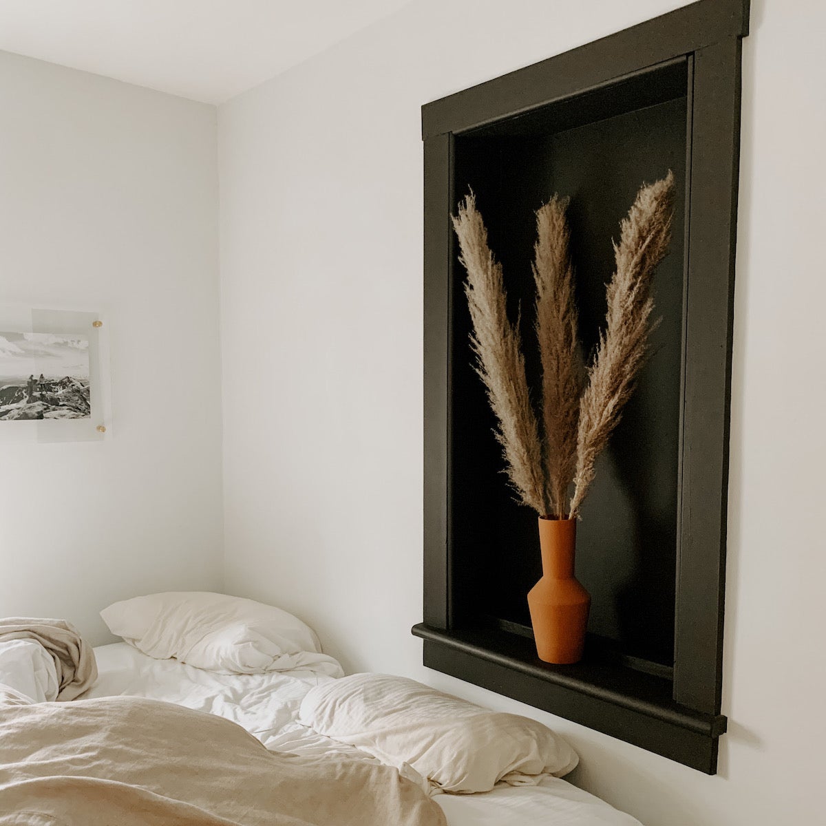 A bedroom with dried florals in a vase on one wall and an acrylic frame on the other.