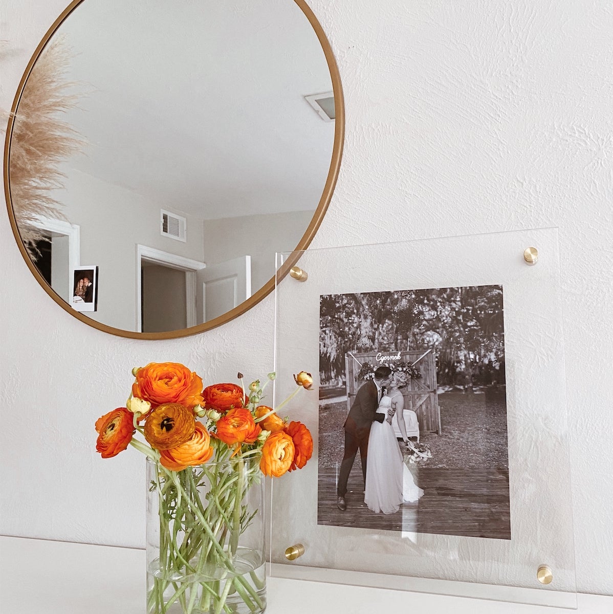 A gold mirror and floating frame are displayed next to a bouquet of orange flowers.