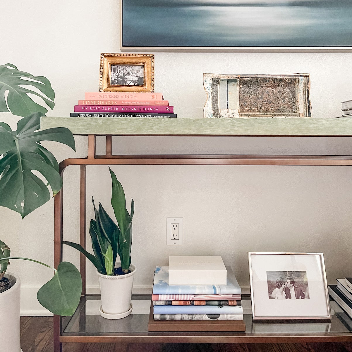 An accent table styled with layers of books, frames, and plants.