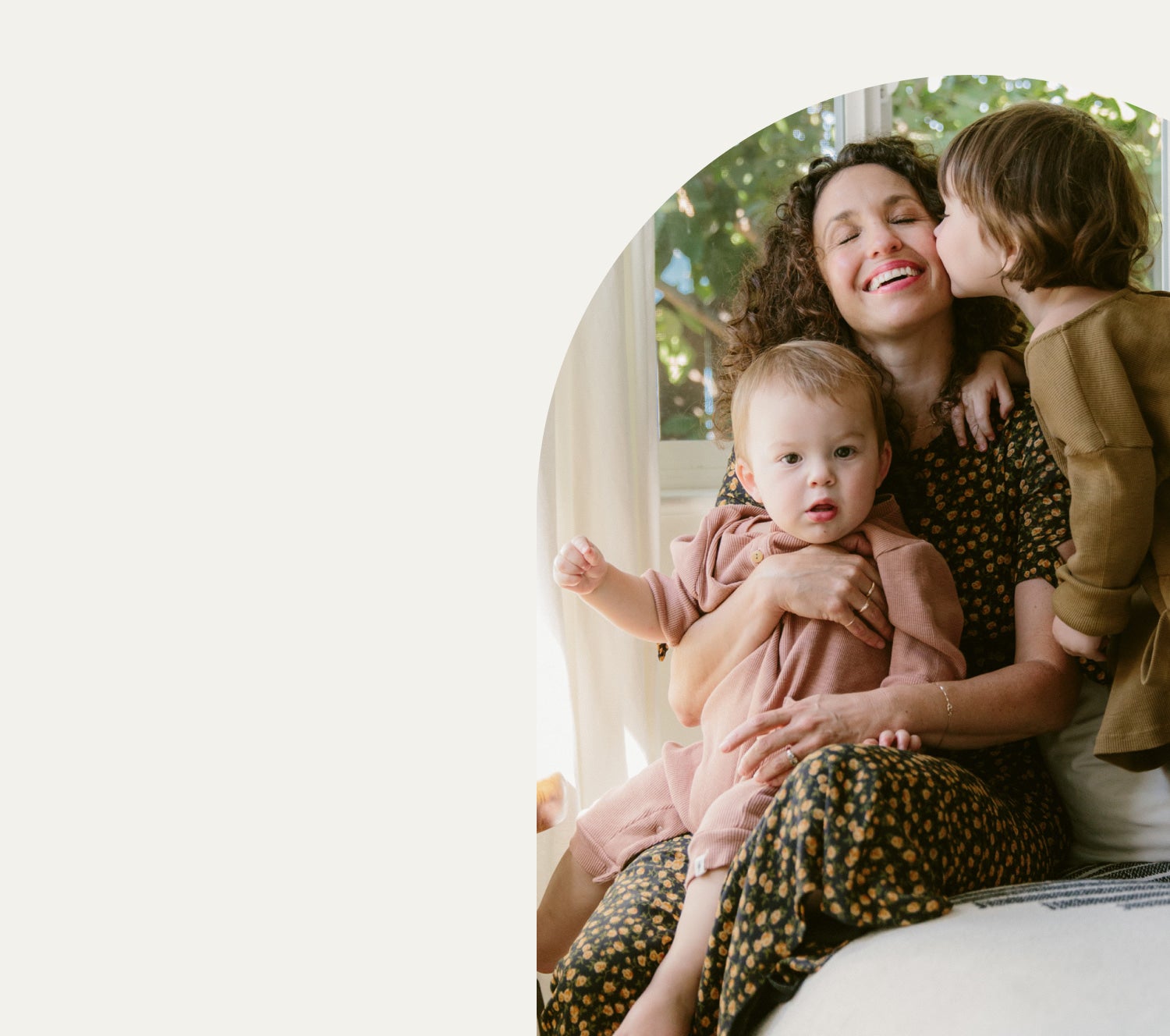Mother holding a baby and getting a kiss on the cheek from her toddler