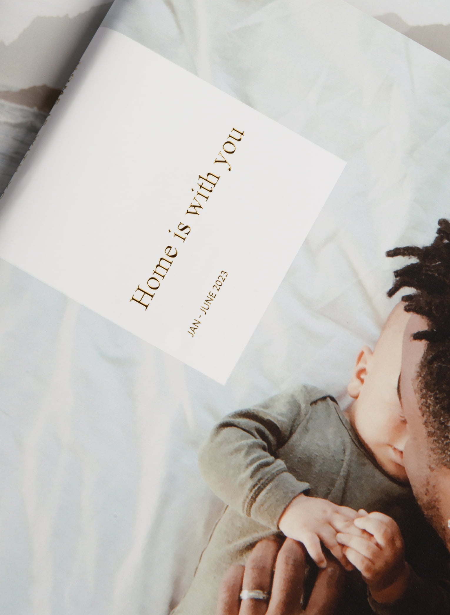 Hardcover Photo Album showcasing gold foil text that reads, “Home is with you Jan - June 2023” Featuring father cuddling baby