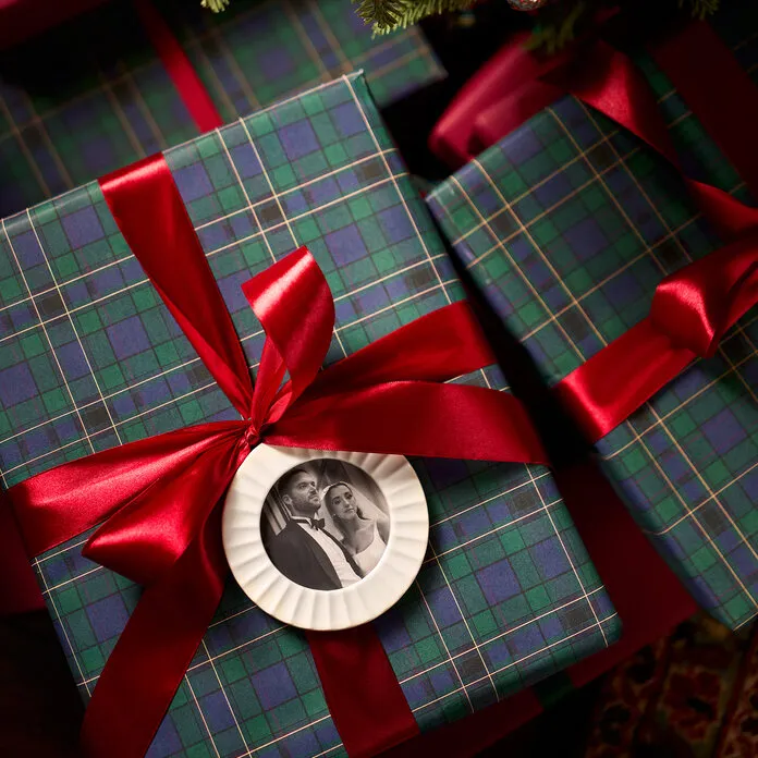 Plaid-wrapped holiday gifts tied with red ribbon and a ceramic photo ornament