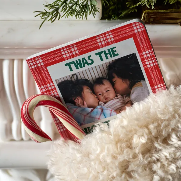 A red plaid family photo book tucked into a cozy blanket with a candy cane