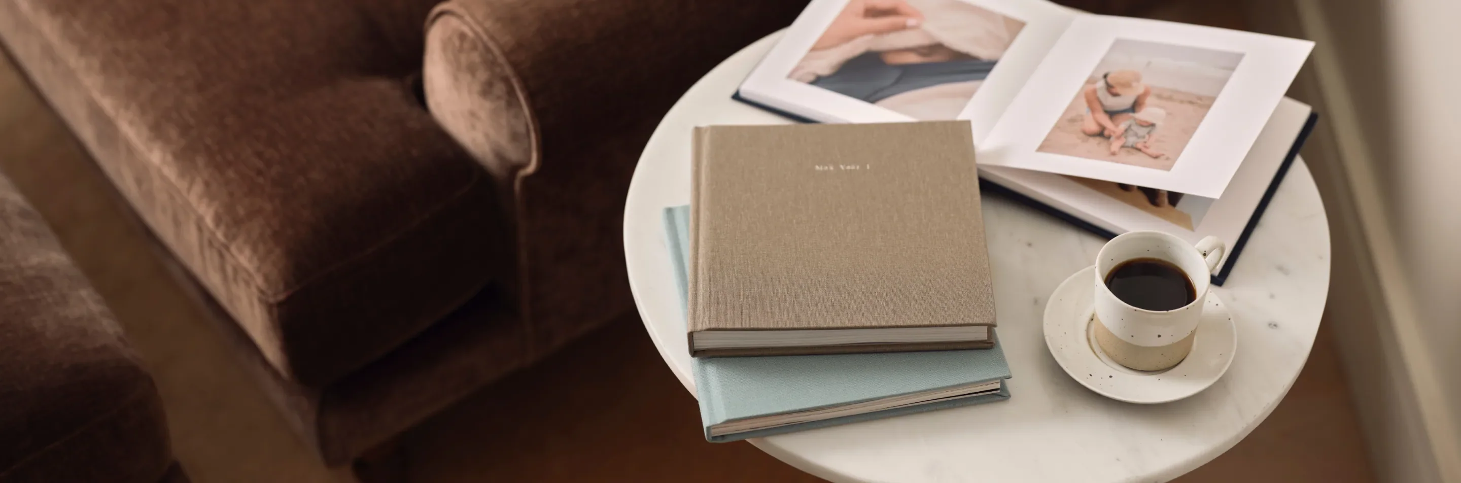 Photo books and coffee on a table beside a brown armchair