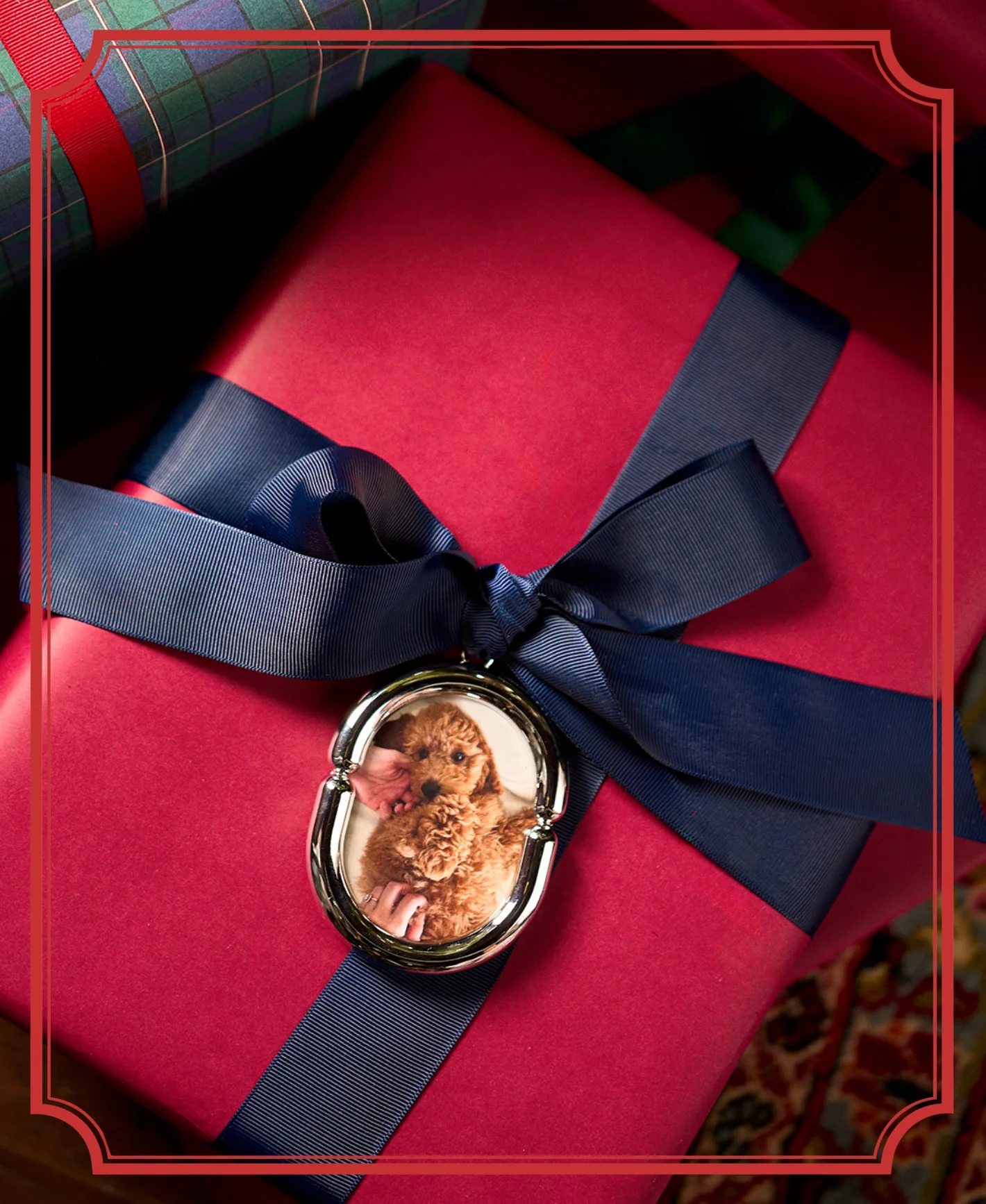 A chrome photo ornament tied to a red gift box with a navy ribbon