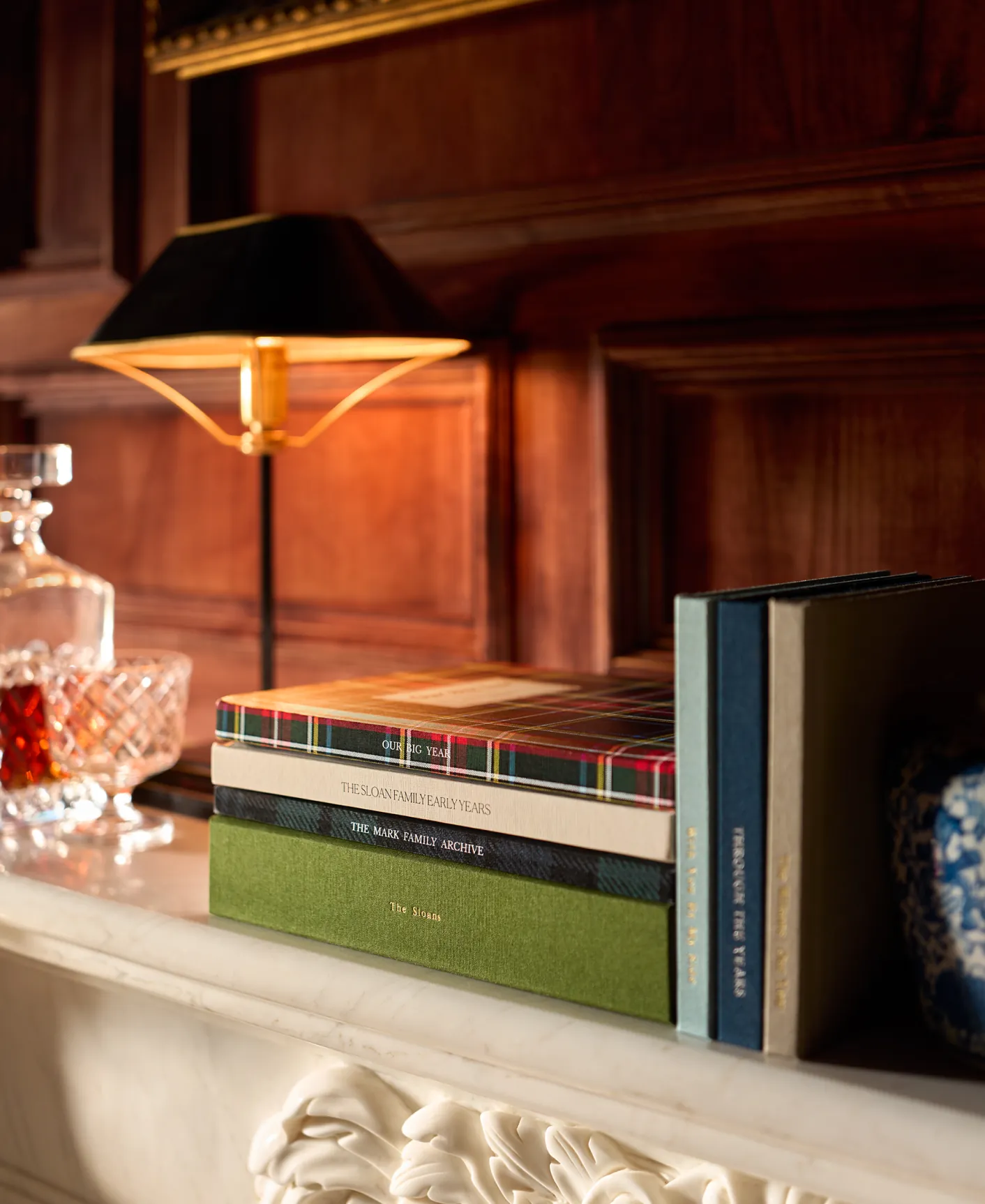 Linen photo albums arranged on a marble mantel beside a glowing lamp