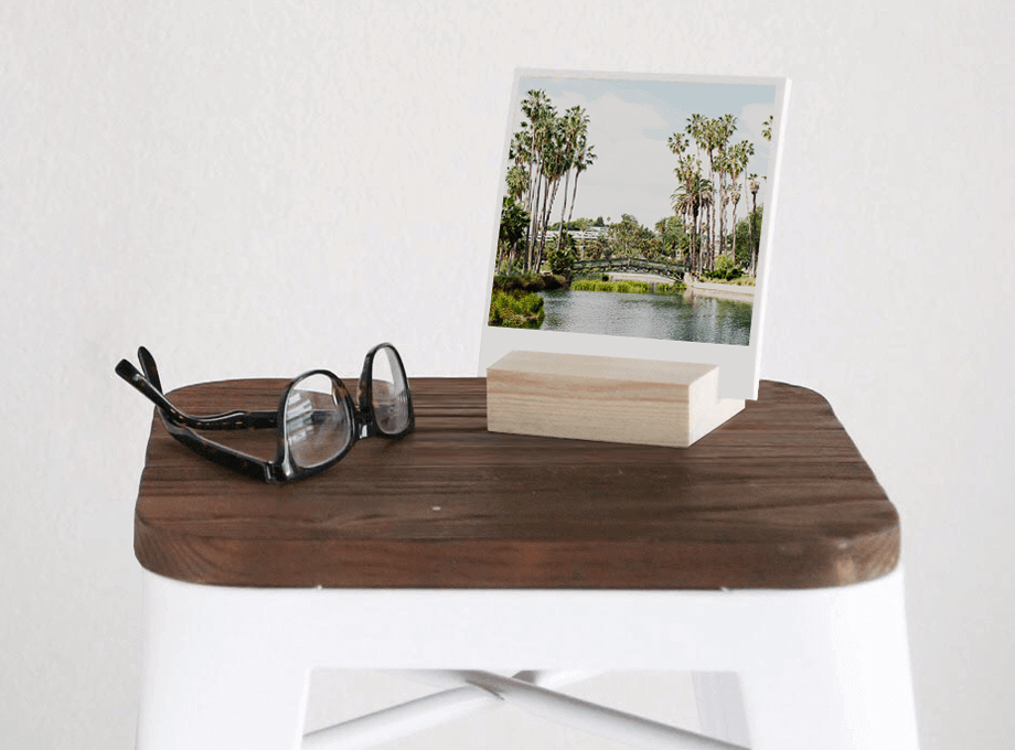Photo prints held by wood block next to eyeglasses on stool