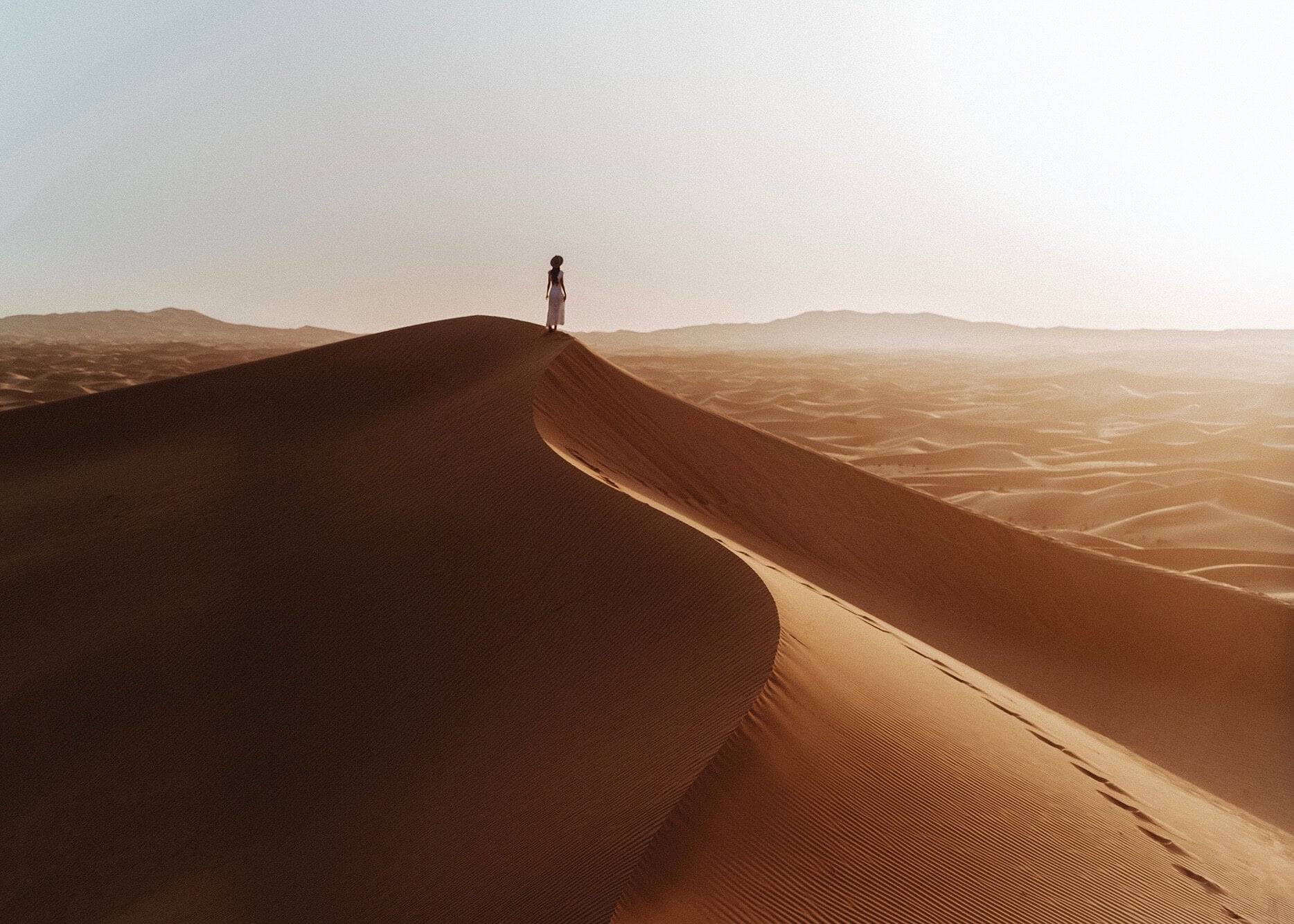Emilie Ristevski photo of woman standing on top of sand dune facing away from the camera at golden hour