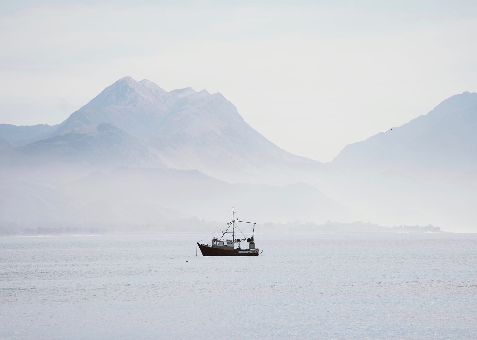 Photo of small boat in front of mountains and rolling fog