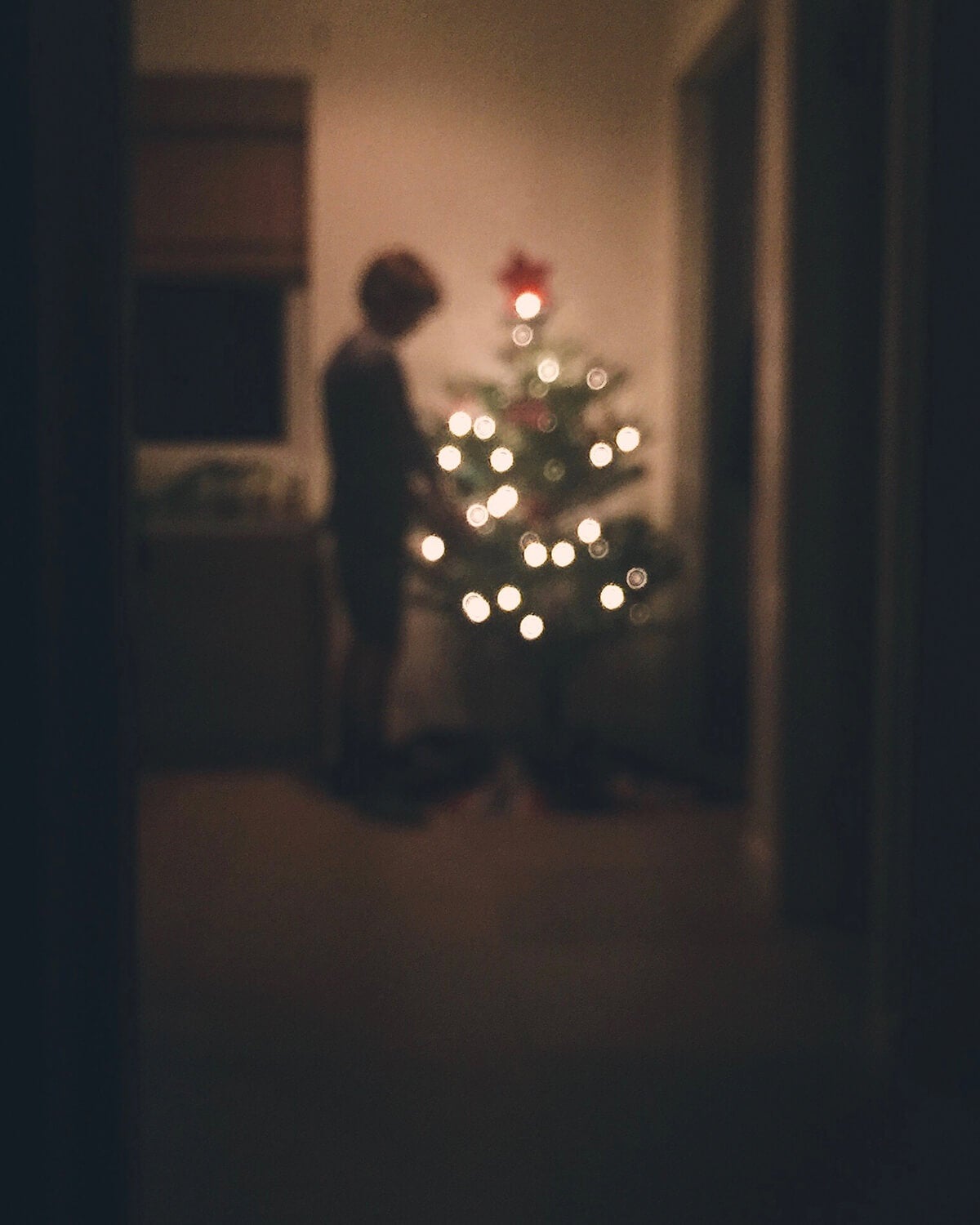 Blurry image of boy standing next to tree in the dim light of the glow from the string lights