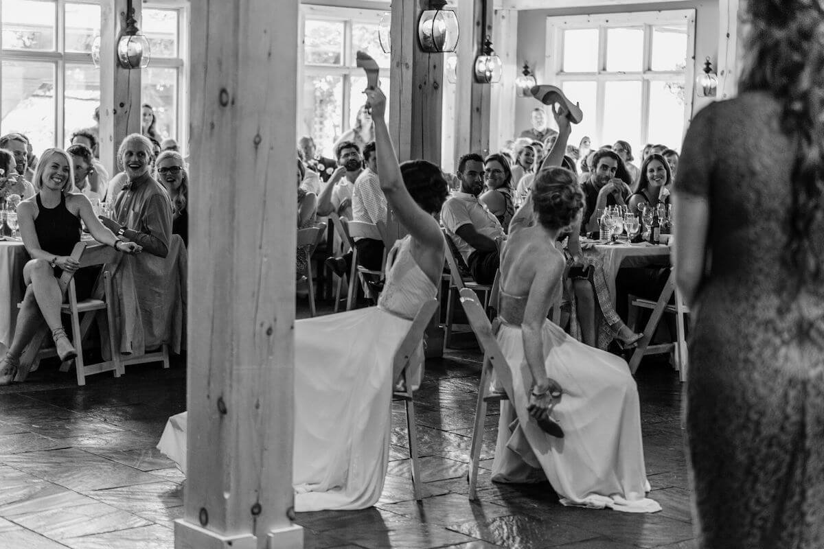 Bridesmaid and bride sitting back to back holding up shoes