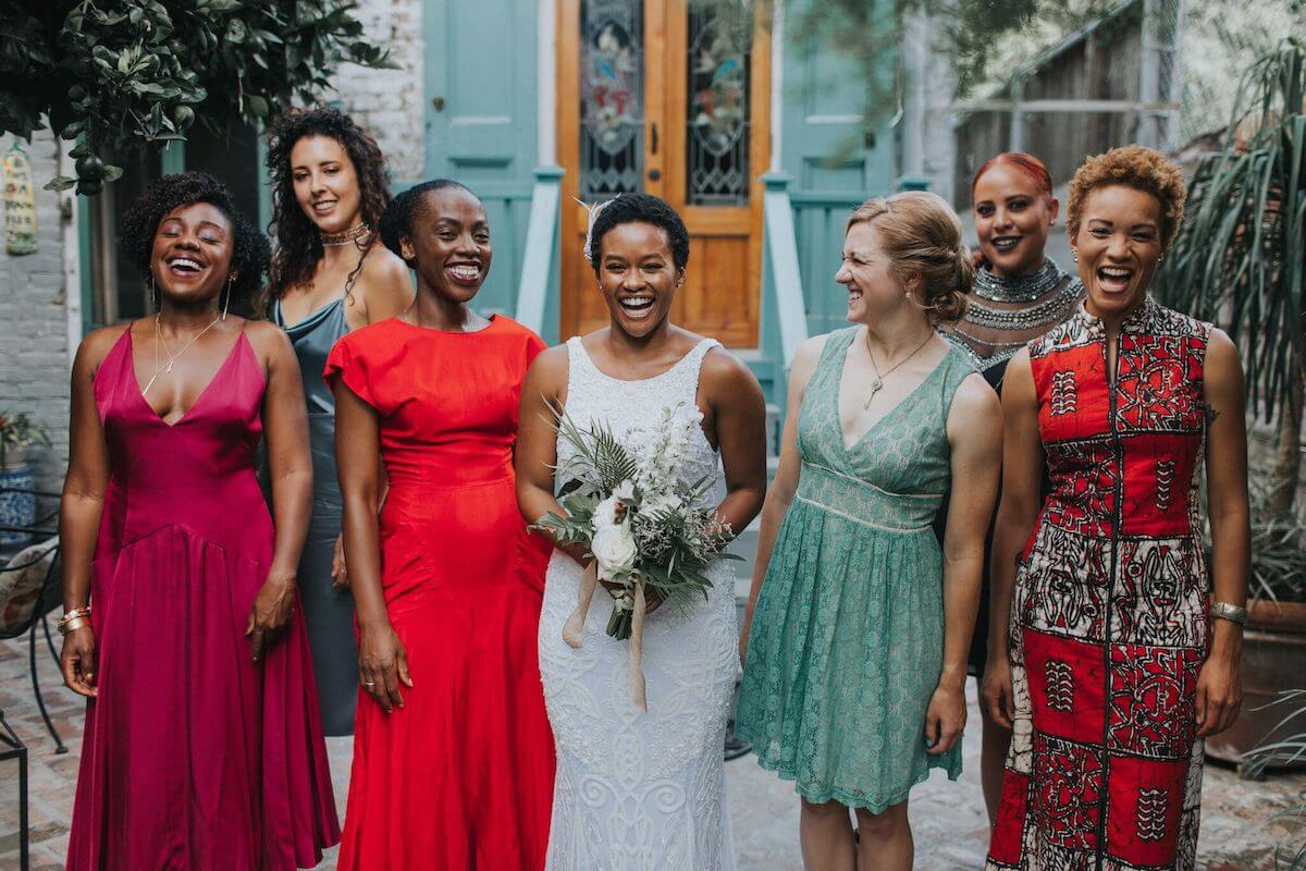 Bridesmaids in vibrant mismatched dresses standing next to bride outside of venue