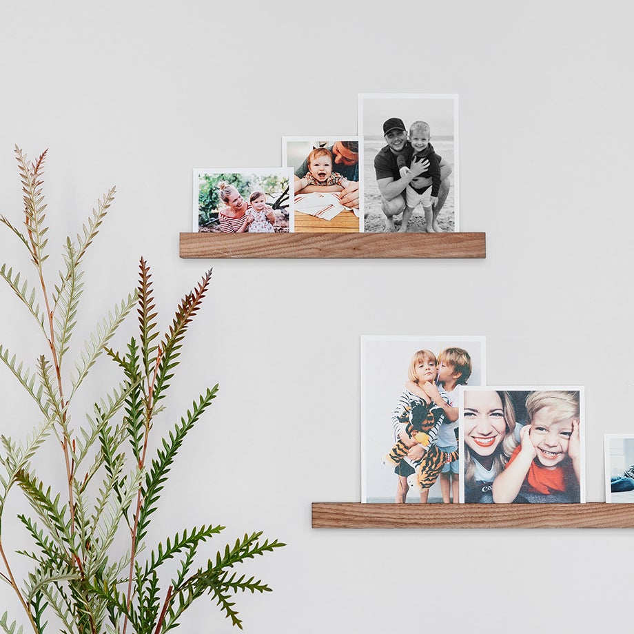 Photo prints of different sizes lined up on two offset wooden photo ledges