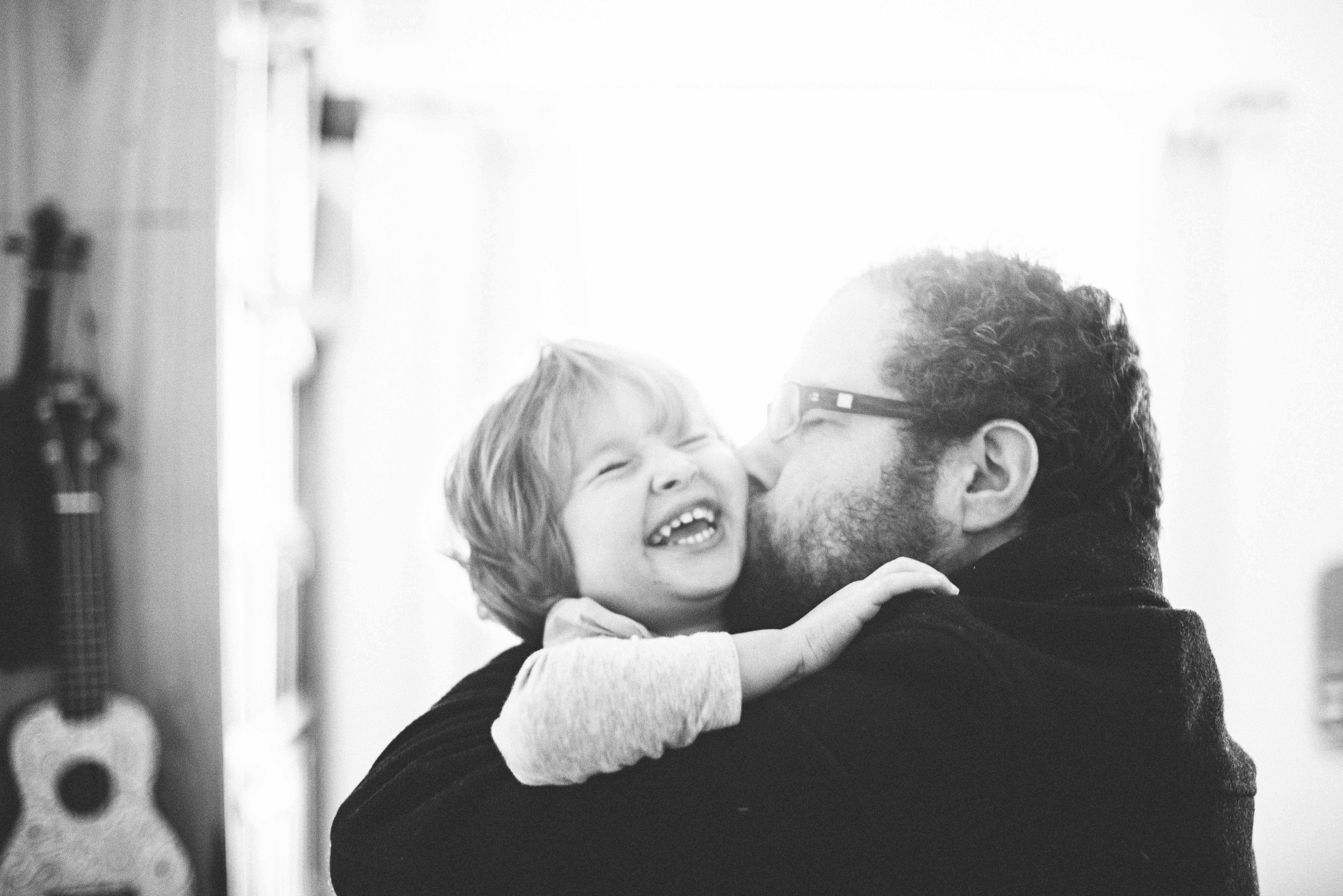 Black and white photo of father kissing little girl on cheek while she laughs