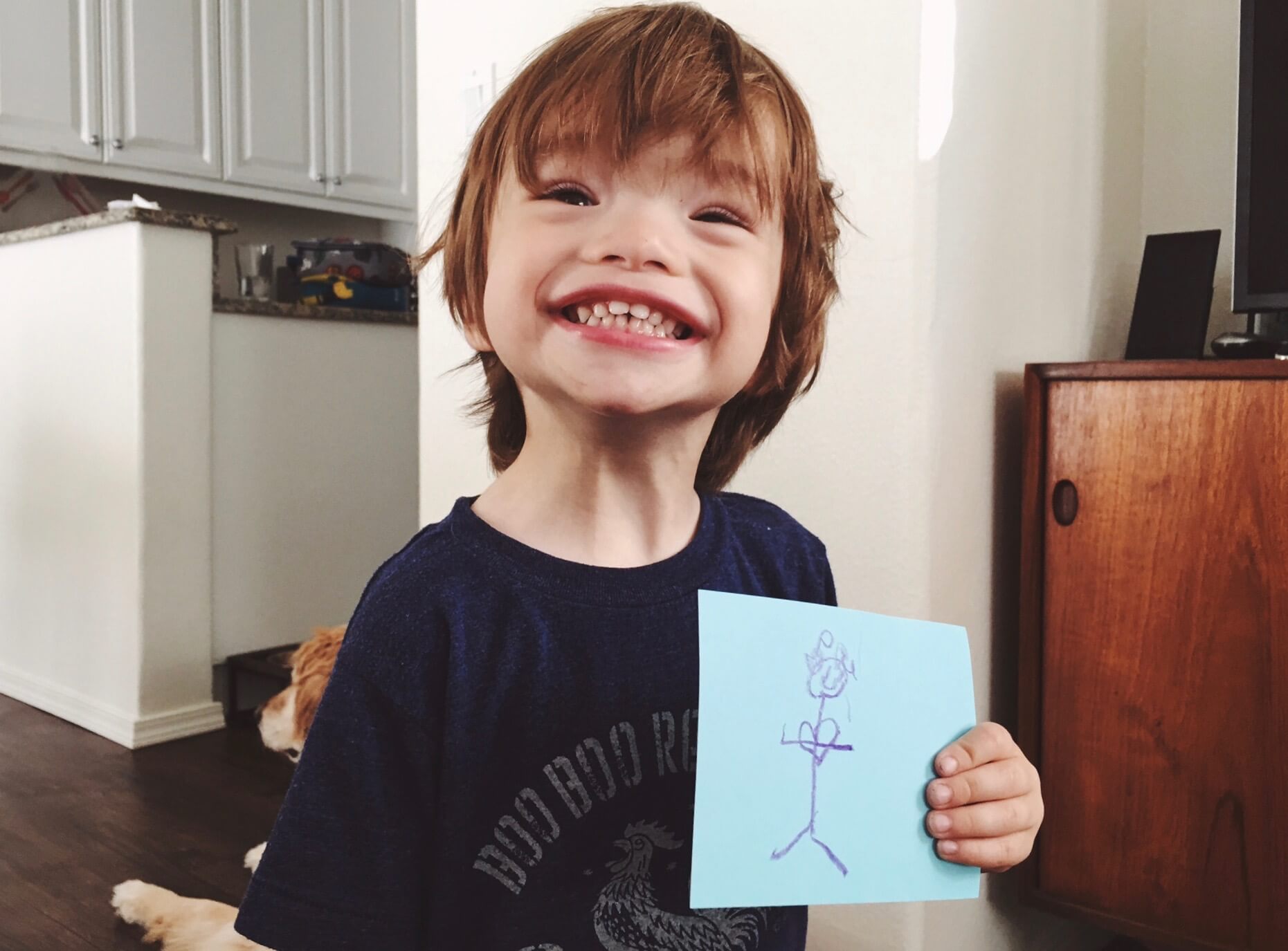 Little boy holding up artwork and smiling proudly