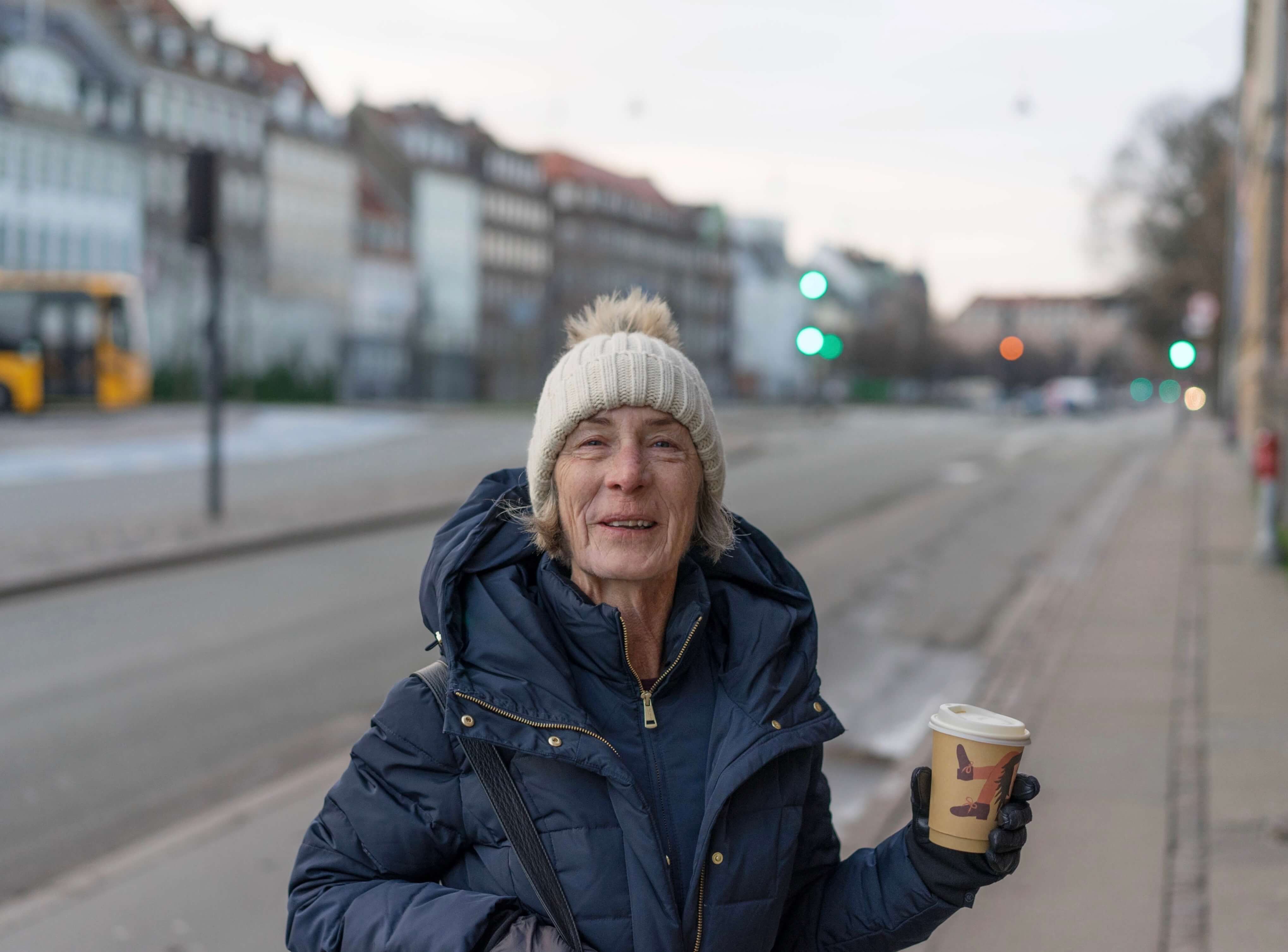 Woman bundled up in large jacket holding coffee cup with surprised smile on her face