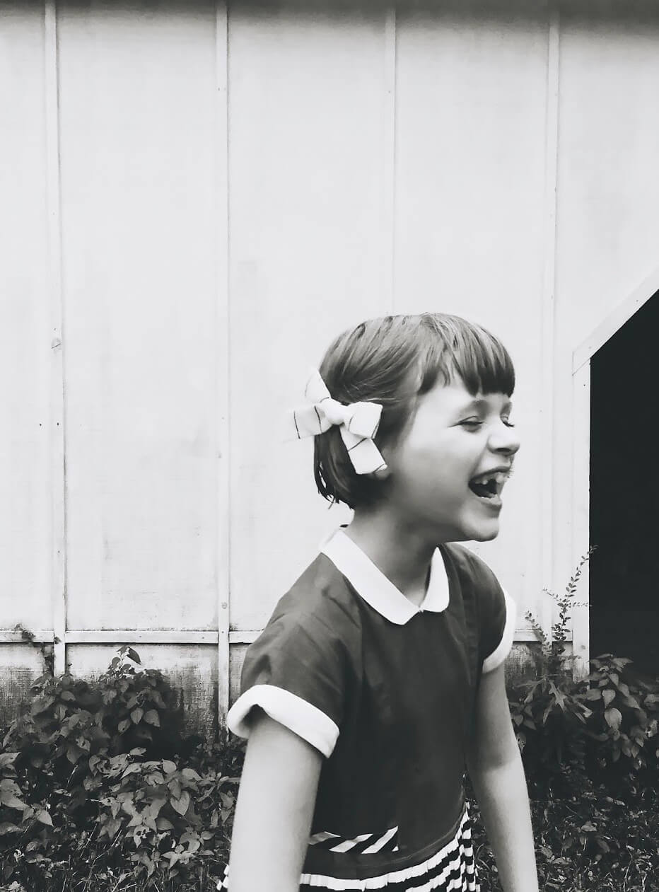 Black and white photo of little girl with bow in her hair laughing